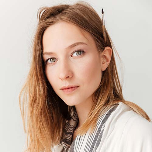 Image of concentrated young caucasian lady painter at workspace. Looking at camera.