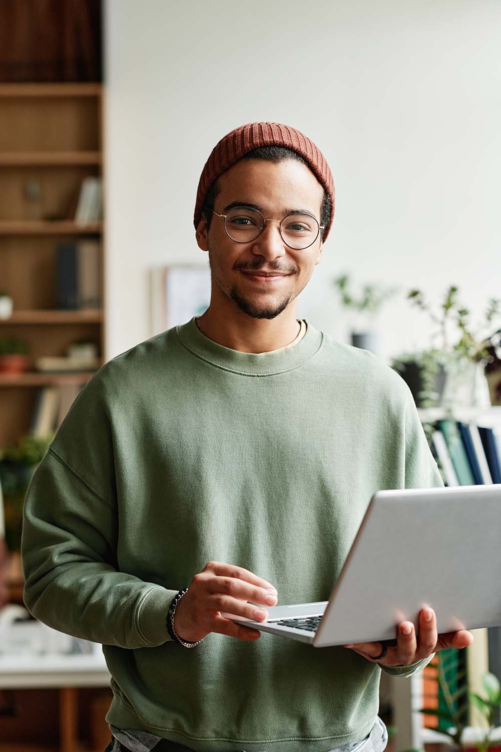 Young confident IT engineer in casualwear looking at camera in office while using laptop and working with online or coded data